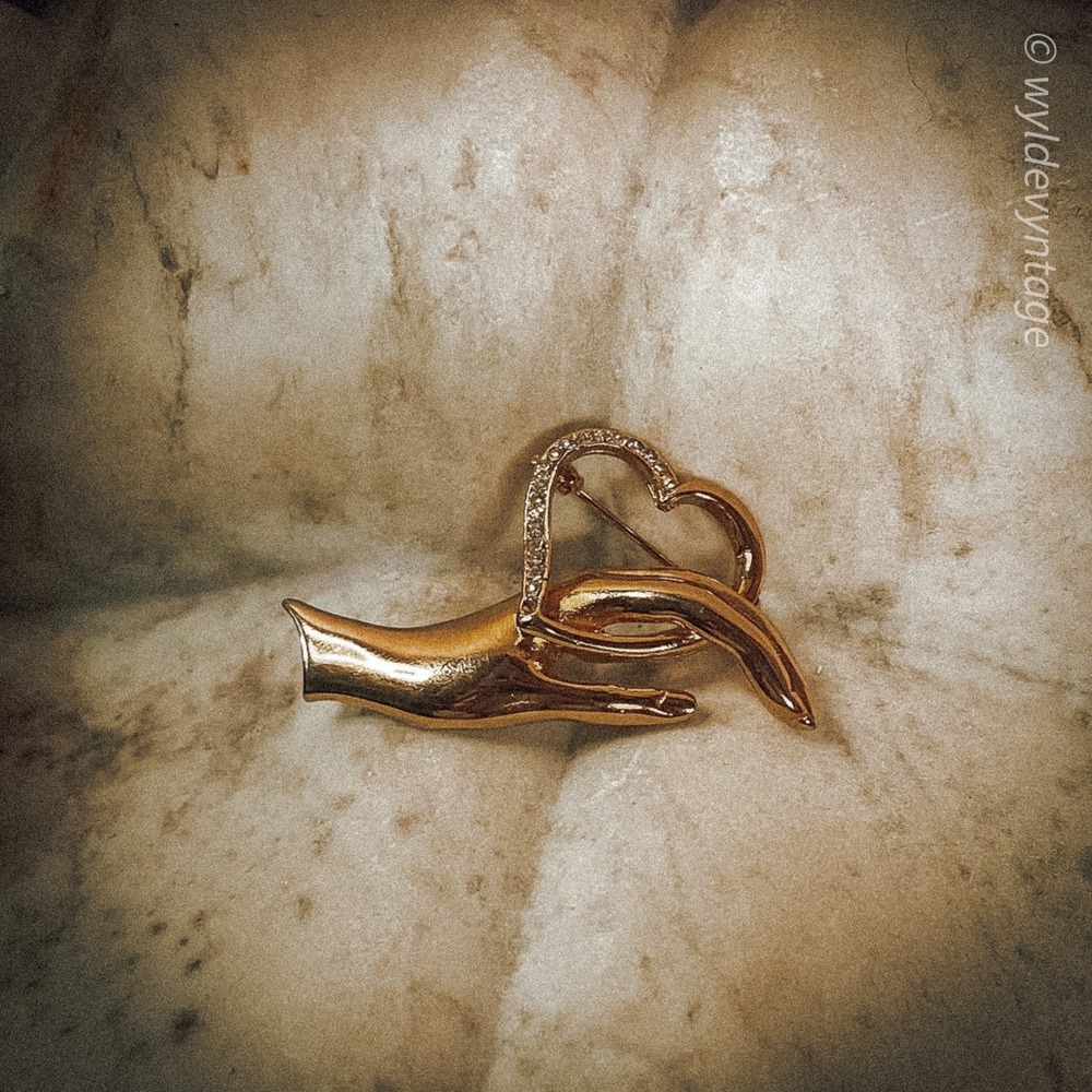 Gold tone hand brooch with a heart and clear stones